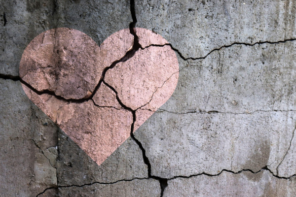 A pink heart on buckling, cracked concrete; concept is broken heart 